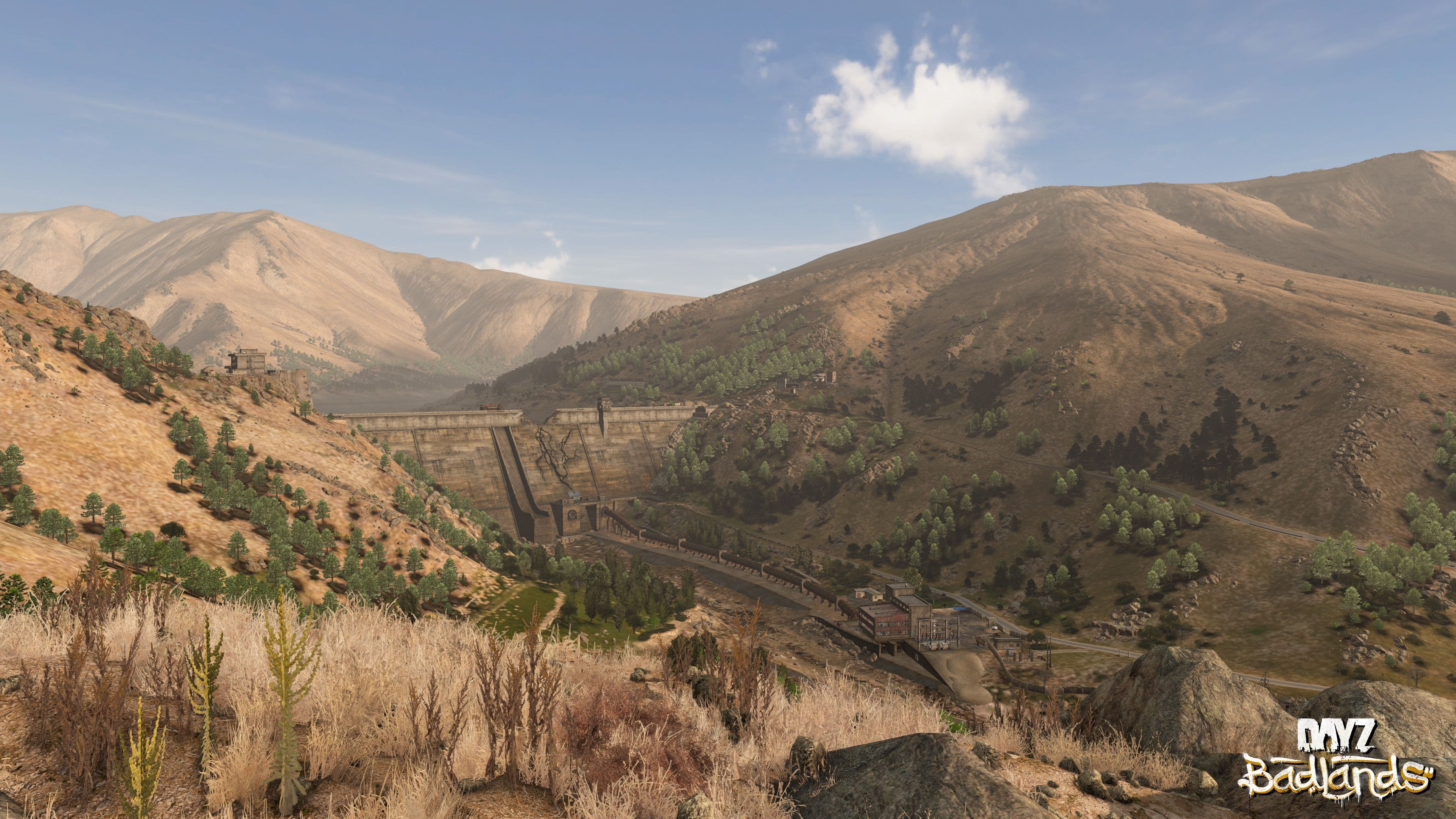 A dam wall spanning a dry valley in Nasdara, with greenery only along the old channel below