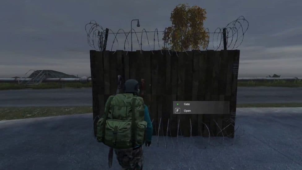 A player-built wooden gate in DayZ topped with barbed wire, showing the Open interaction prompt