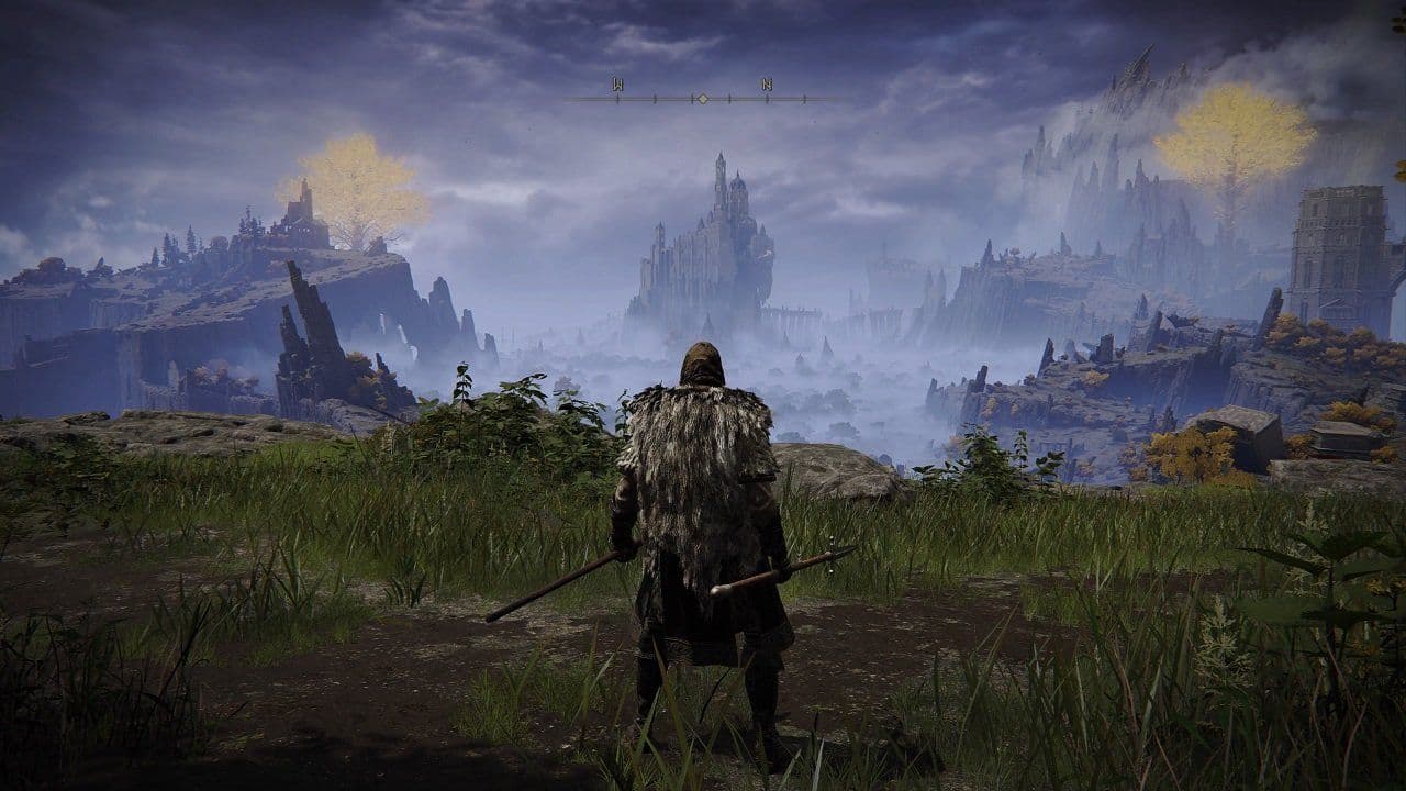 A lone figure stands on a hilltop viewing the foggy mountains and ancient ruins of Elden Ring.