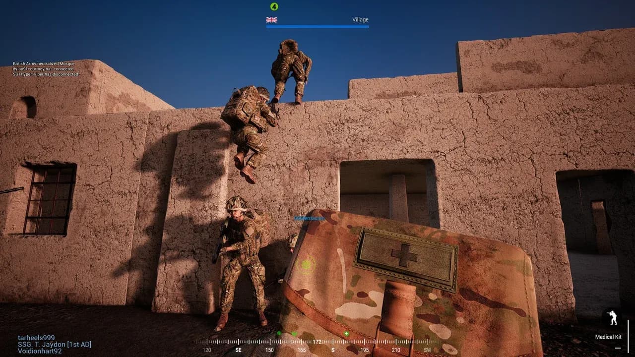 Three British Army soldiers in Squad clearing a mud-brick compound wall one after another — one already standing on the flat roof, one mid-climb with hands on the parapet, one waiting at the base.