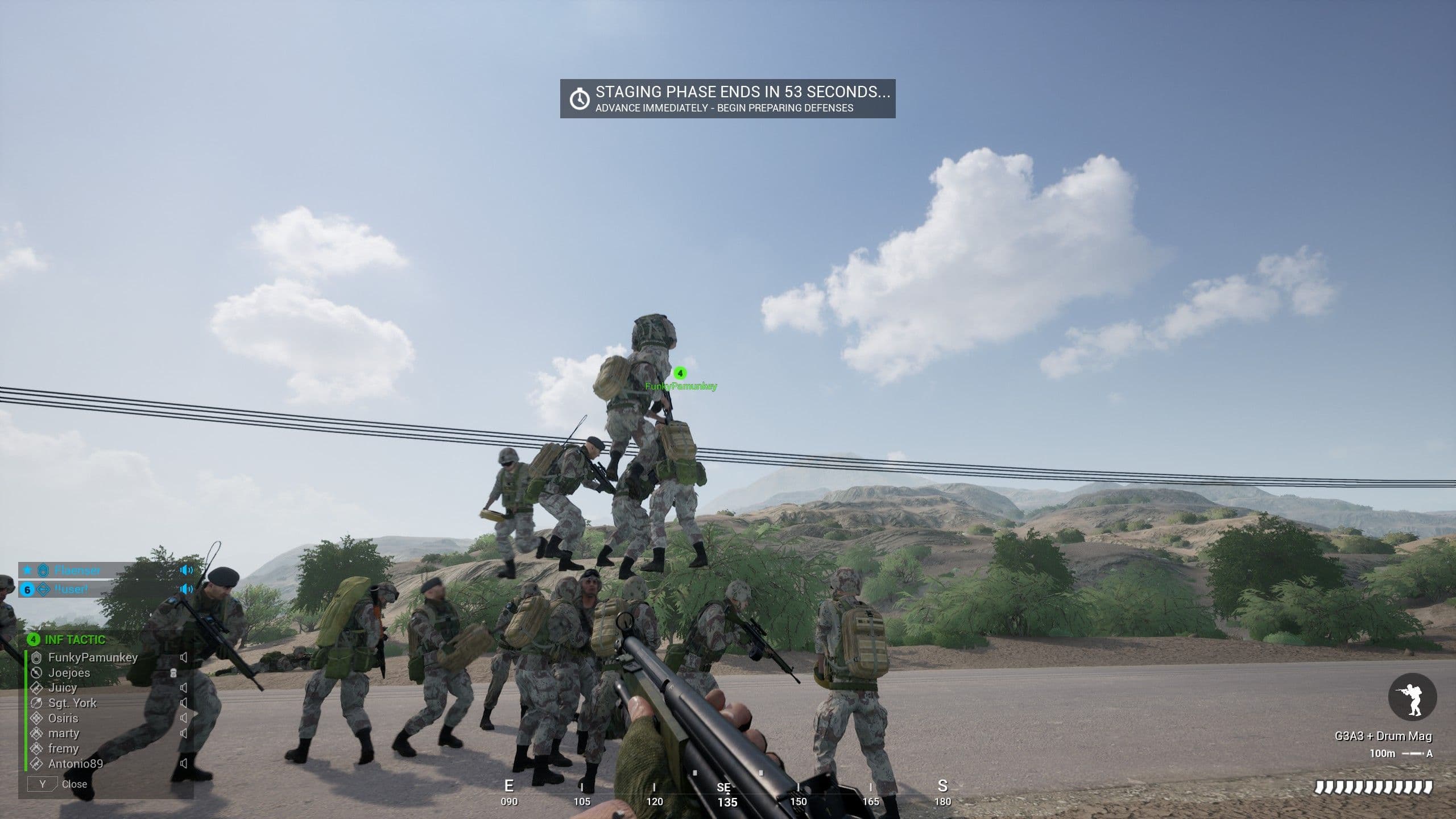 Squad players stacked several bodies high on an open road during a match's staging phase, thirteen months after the Infantry Combat Overhaul shipped — standing on a teammate still works.